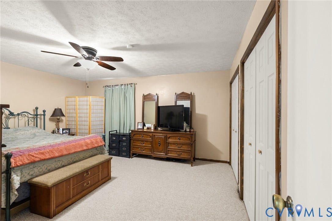Carpeted flooring, ceiling fan with integrated lighting, window with drapes, and two bi-fold closet doors with wood trim