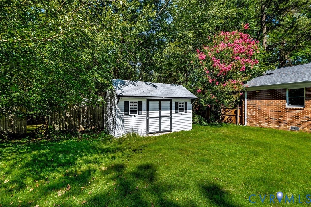 13012 Harrowgate Road, Chesterfield, VA 23831 Expansive green lawn featuring a white storage shed with black shutters, a brick exterior wall, and mature trees