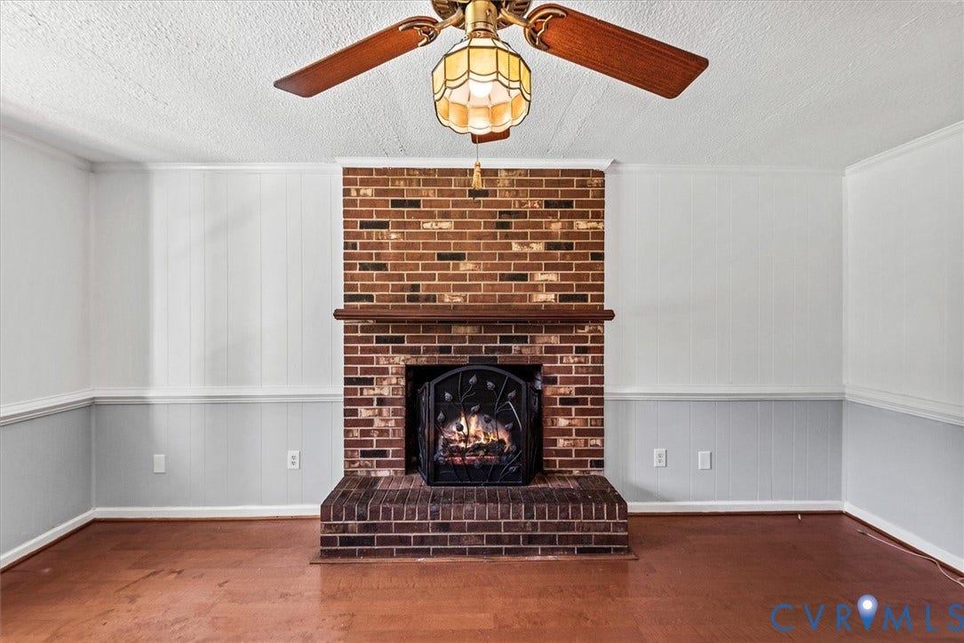 13012 Harrowgate Road, Chesterfield, VA 23831 Brick fireplace with a wooden mantel and decorative screen, wood-finish flooring, and a ceiling fan with an integrated light fixture