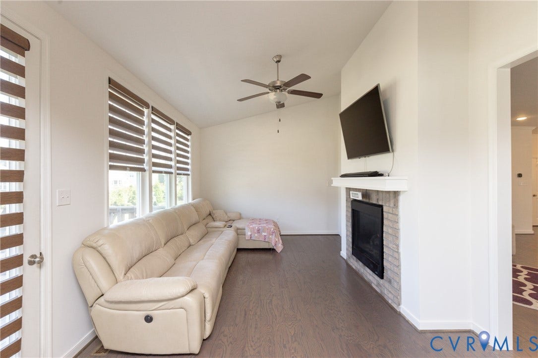 Vaulted ceiling with a ceiling fan, fireplace with a white brick surround, dark wood-finish flooring, and multiple windows