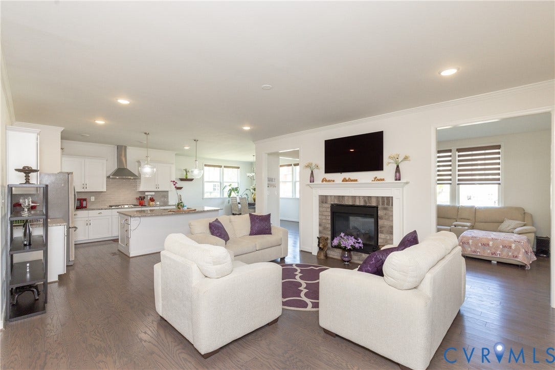 Open-concept living space featuring wood-finish flooring, a kitchen with an island, white cabinetry, and a brick fireplace
