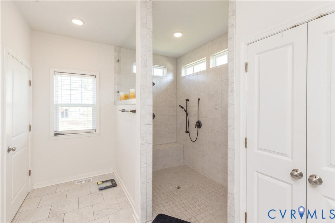 Spacious shower with tiled walls, built-in bench, and dual shower heads