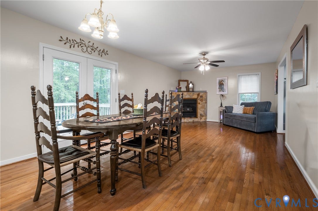Hardwood flooring throughout, stone-clad fireplace, ceiling fan with integrated lighting, double French doors, and a decorative chandelier