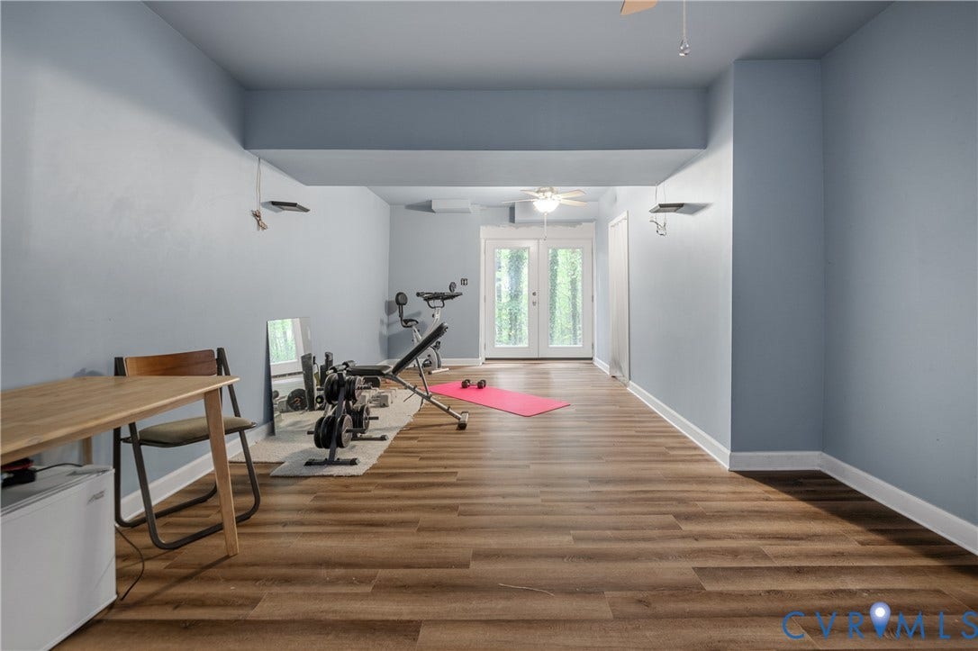 Wood-finish flooring throughout, light blue wall paint, white trim, recessed ceiling with a ceiling fan, and double French doors to the exterior
