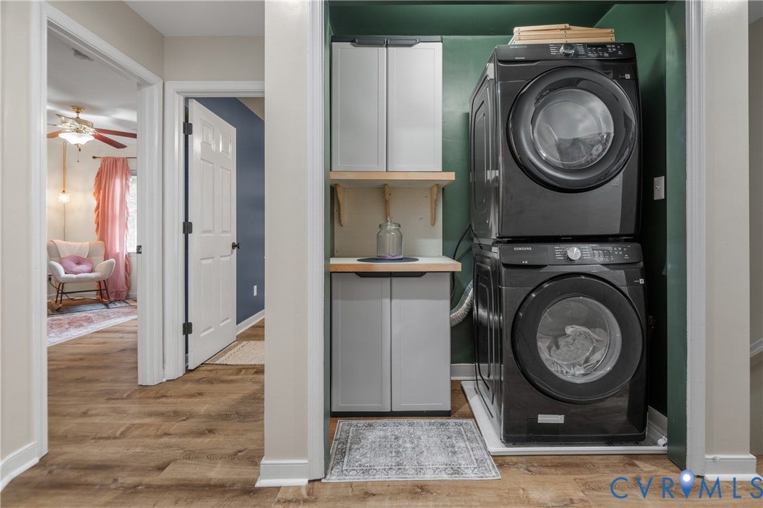 Integrated laundry area featuring stacked black appliances, wood-finish flooring, and built-in shelving