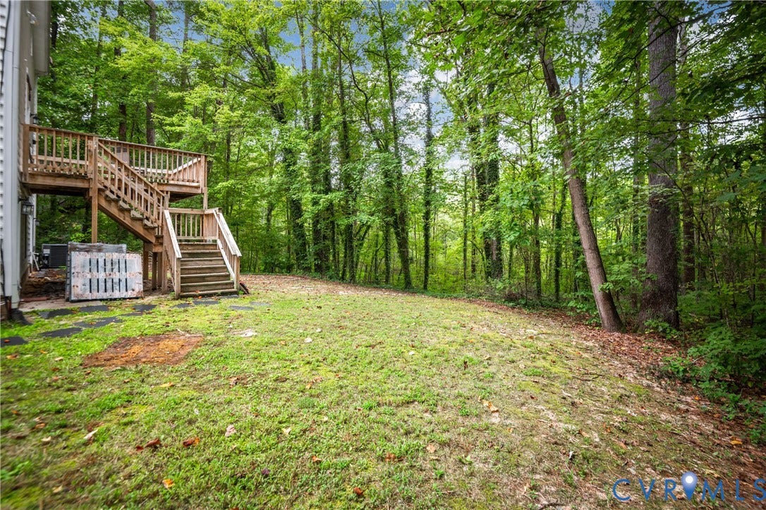 Expansive outdoor space featuring a two-story wood deck with railings, integrated wood stairs, and a surrounding wooded landscape