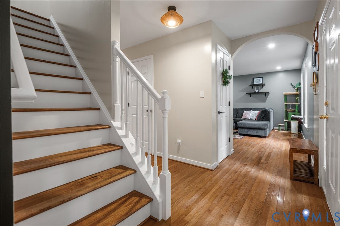 Hardwood flooring throughout, white painted staircase with wood treads, arched entryway, and recessed lighting