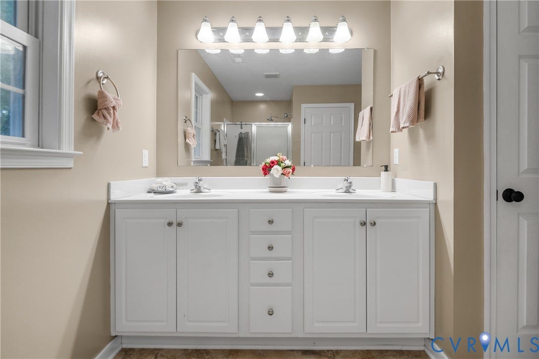 Dual vanity with white cabinetry, integrated sinks, chrome fixtures, and a large wall-mounted mirror