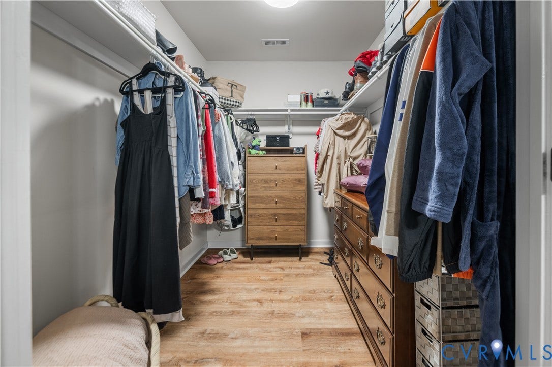 Walk-in closet with wood-finish flooring, built-in shelving, and hanging rods