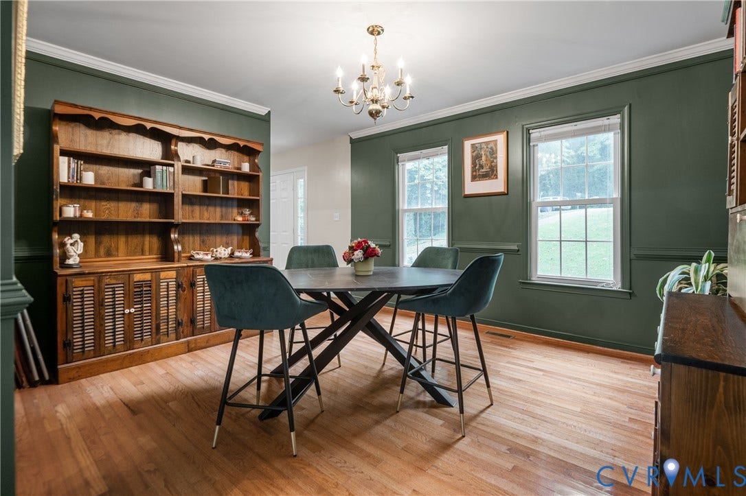 Hardwood flooring, painted walls with wainscoting, crown molding, and a chandelier lighting fixture