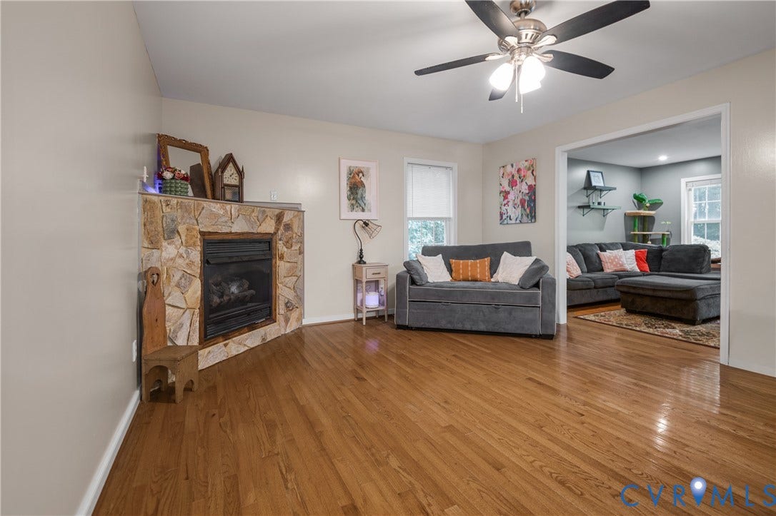 Hardwood flooring, a stone-clad fireplace, and a ceiling fan with integrated lighting