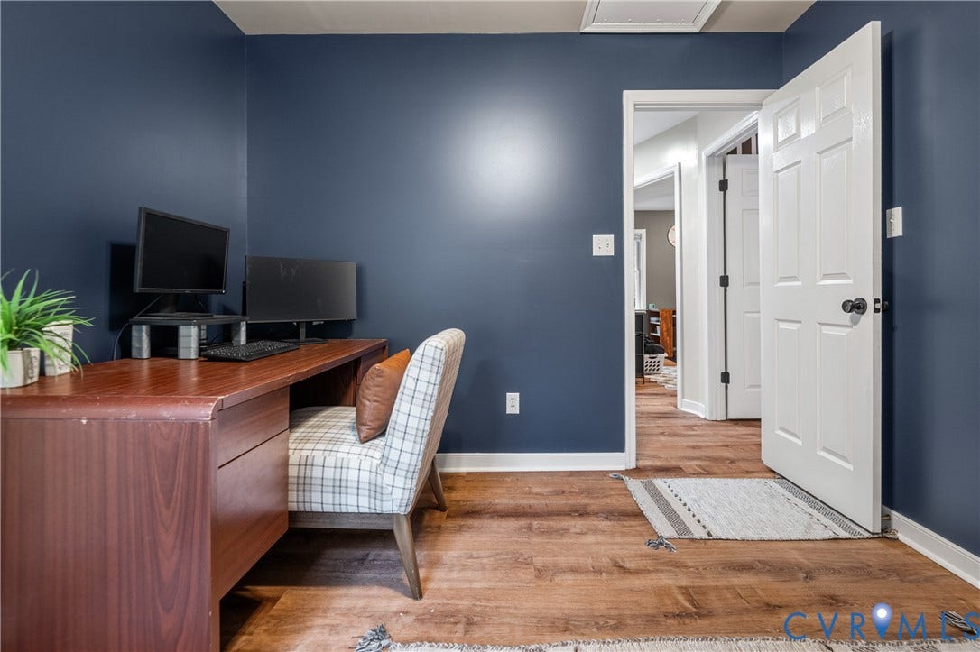 Wood-finish flooring, deep blue wall paint, white trim, and a white panel door with black hardware