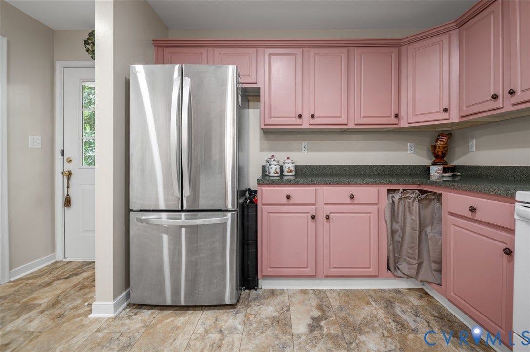 Wood-finish flooring, stainless steel refrigerator, pink cabinetry, dark countertops, and a paneled door with glass insert