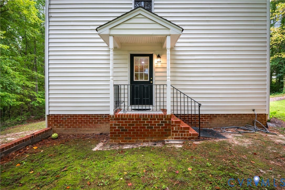 Covered entry featuring white siding and brick foundation