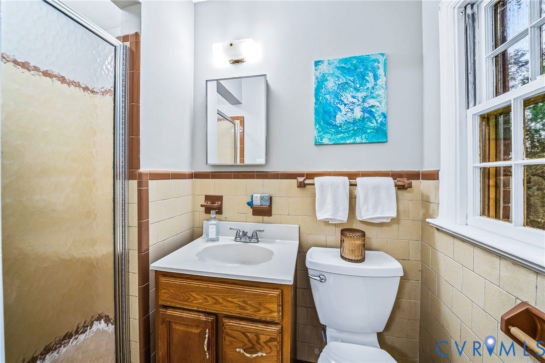 7548 Piney Branch Road, Stratford Hills, Richmond, VA 23225 Frosted glass shower enclosure, wood-finish vanity with white countertop, recessed medicine cabinet, wall-mounted light fixture, and tile wainscoting