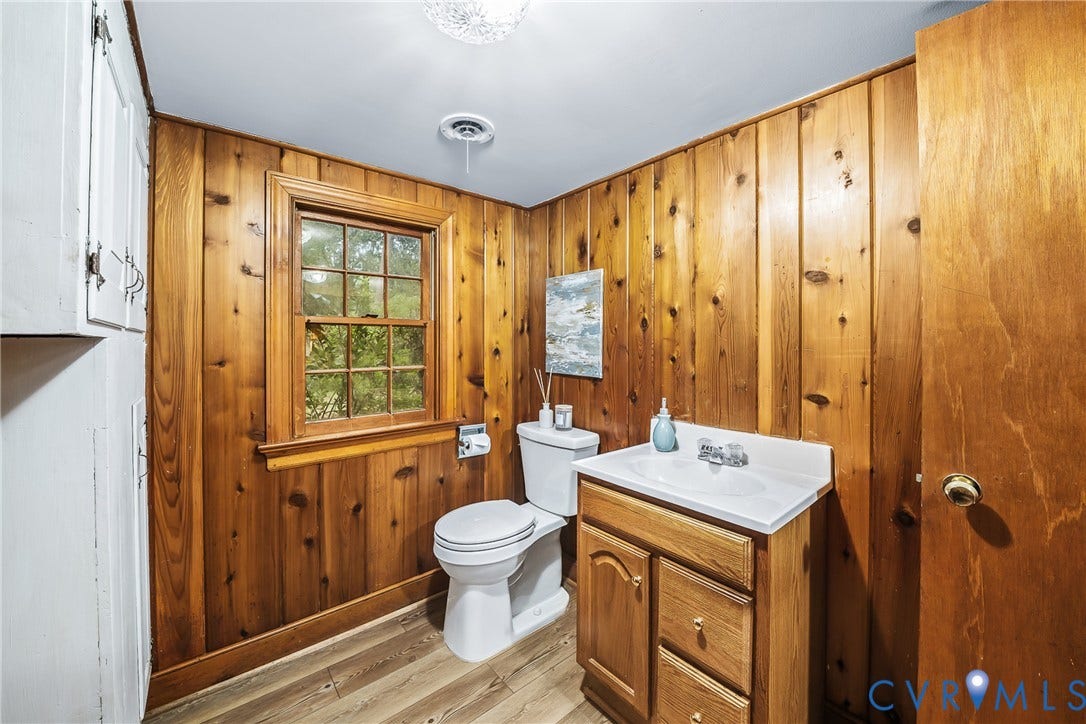 7548 Piney Branch Road, Stratford Hills, Richmond, VA 23225 Wood paneling throughout, white ceiling with flush-mount lighting, wood-finish flooring, white vanity with integrated sink, and a window providing natural light