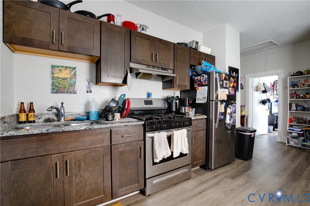 3314 3rd Avenue, Northside, Richmond, VA 23222 Galley kitchen featuring wood-finish flooring, dark wood-tone cabinetry with chrome hardware, a stainless steel gas range, and a stainless steel refrigerator