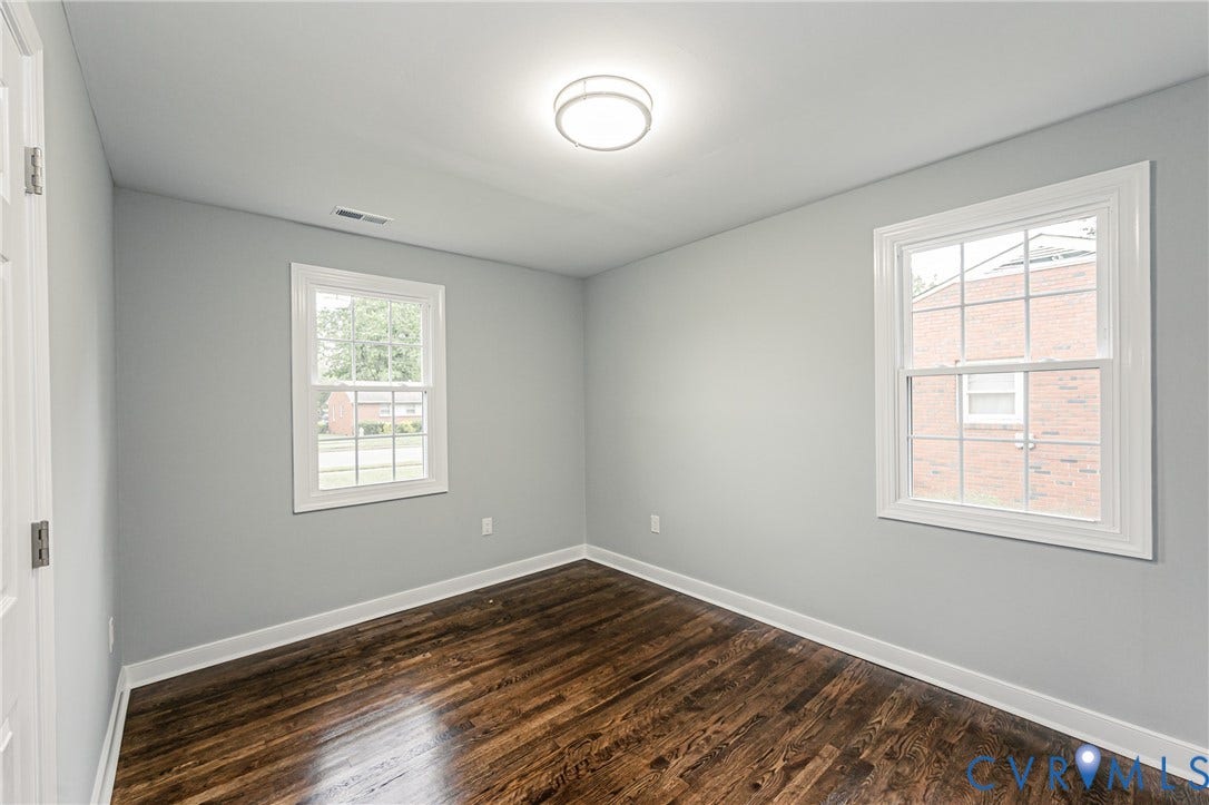 1608 Bryan Street, Richmond, VA 23223 Hardwood flooring, two single-hung windows with white trim, a flush mount ceiling light fixture, and light gray wall finishes