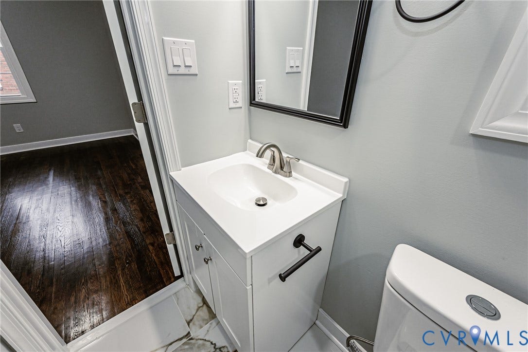 1608 Bryan Street, Richmond, VA 23223 White vanity with a brushed nickel faucet, ceramic sink, and a black-framed mirror