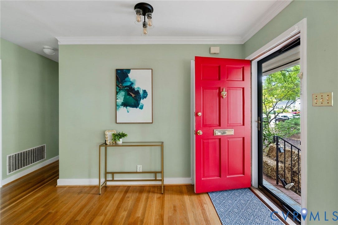 Hardwood flooring throughout the entry, painted paneled door with brass hardware, and a ceiling-mounted fixture