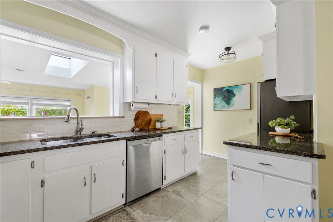 White cabinetry with dark stone countertops, stainless steel appliances, and a pass-through window with a skylight