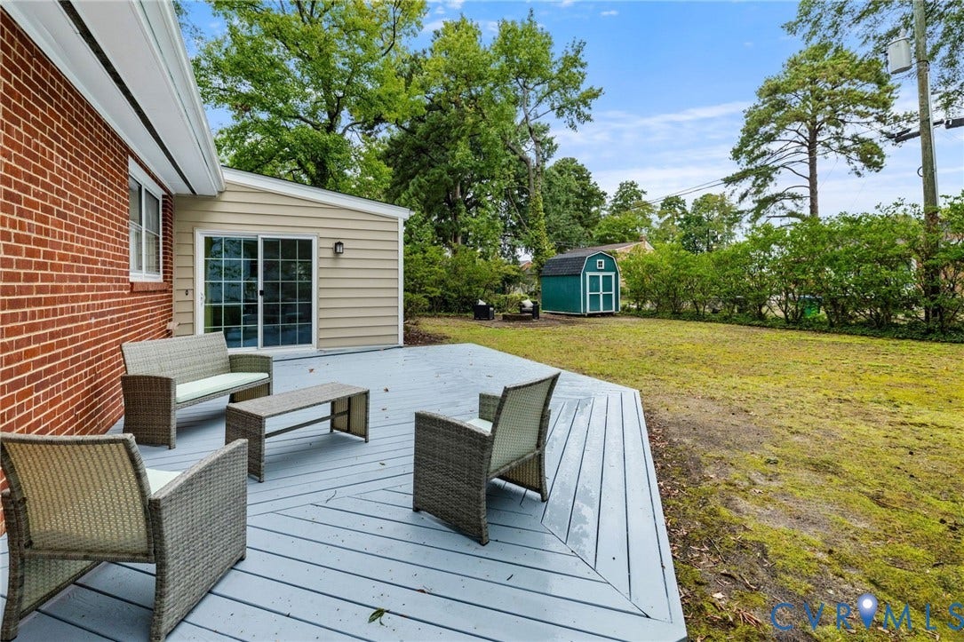 Expansive backyard featuring a gray deck, mature trees, and a storage shed