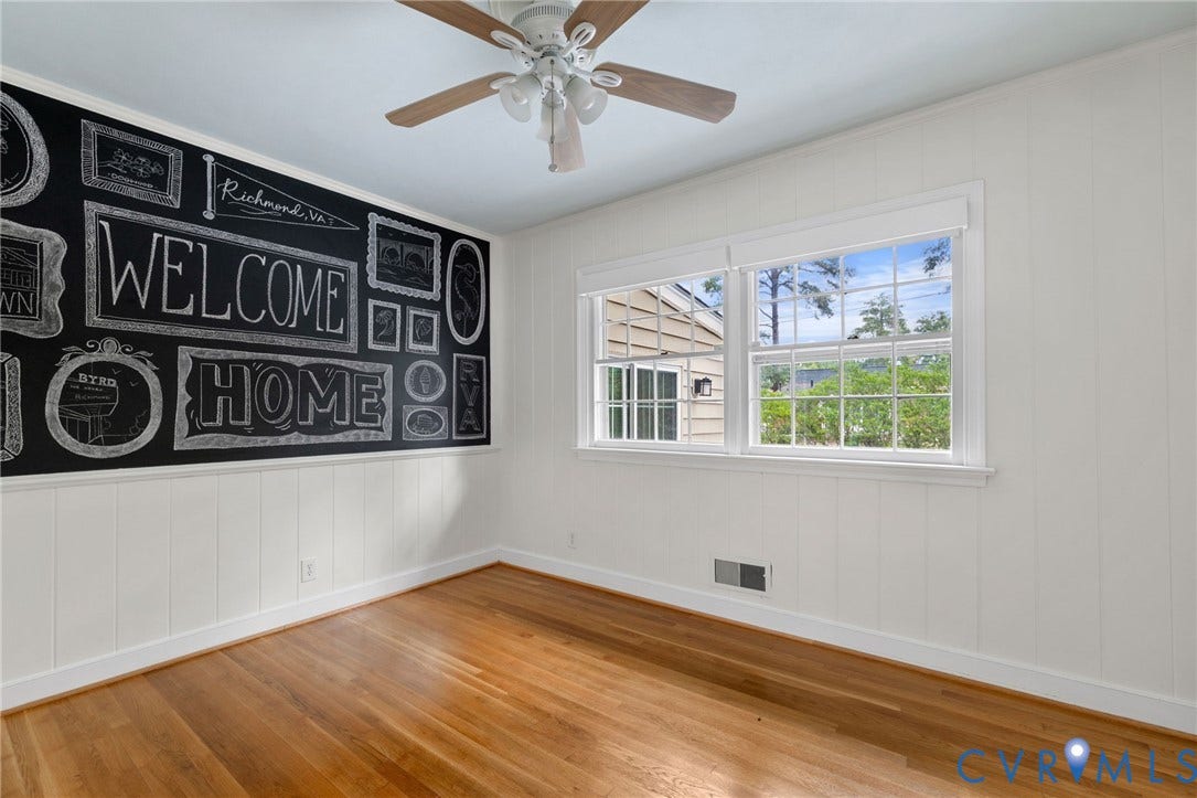 Hardwood flooring, painted paneling, dual windows, ceiling fan, and decorative chalkboard wall
