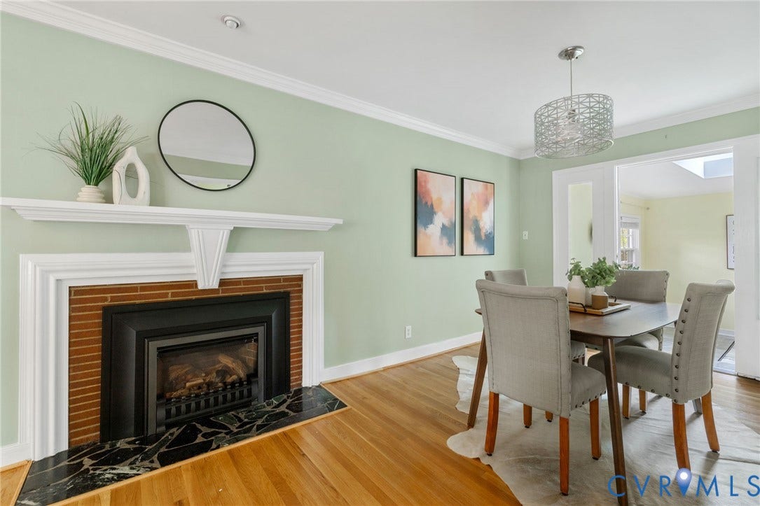 Wood-finish flooring, crown molding, and a fireplace with a black marble hearth and brick surround
