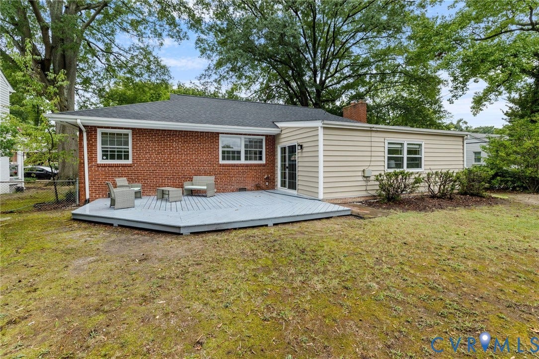 Rear exterior featuring a grey wood-finish deck, brick facade, and tan siding