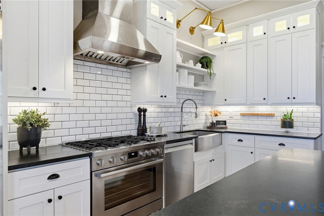 1848 W Grace Street, Historic W. Grace Street, Richmond, VA 23220 White shaker-style cabinetry with black hardware, stainless steel appliances, black countertops, white subway tile backsplash, and a stainless steel farmhouse sink