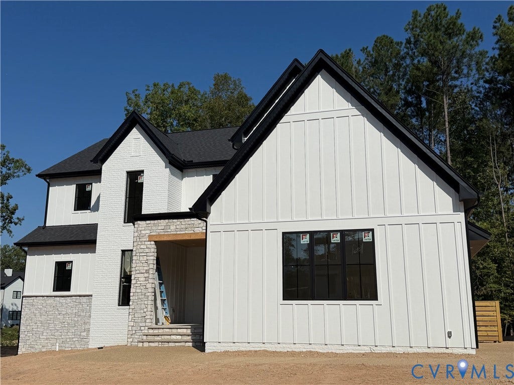 White board-and-batten siding with black trim, black-framed windows, and stone veneer accents