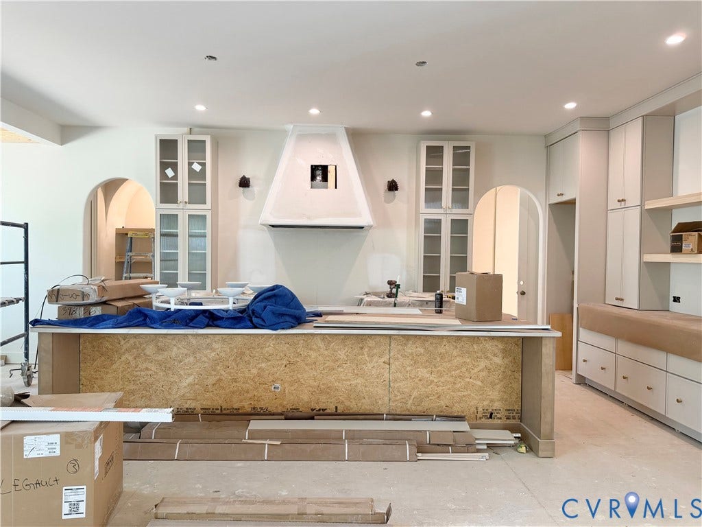 Built-in cabinetry with glass-front uppers, recessed lighting, arched doorways, and a custom range hood