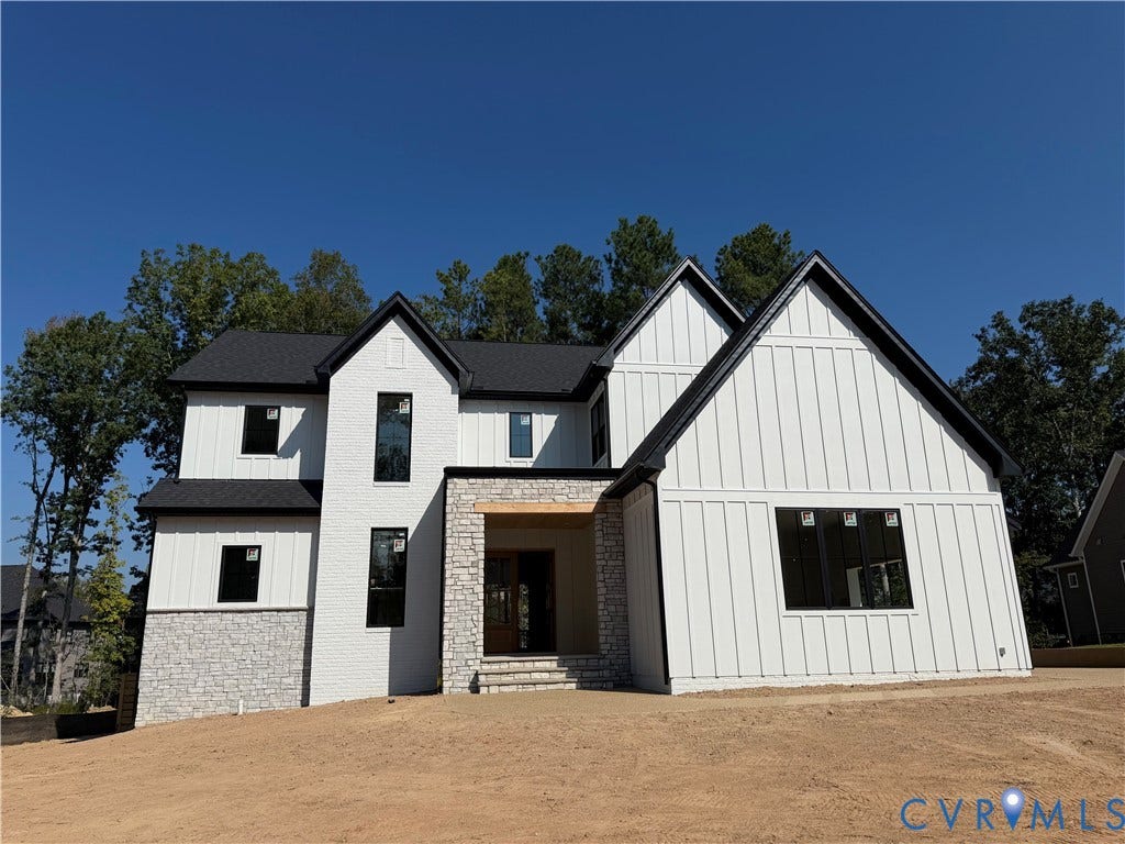 Two-story exterior with white board and batten siding, black framed windows, a dark shingled roof, and stone accents