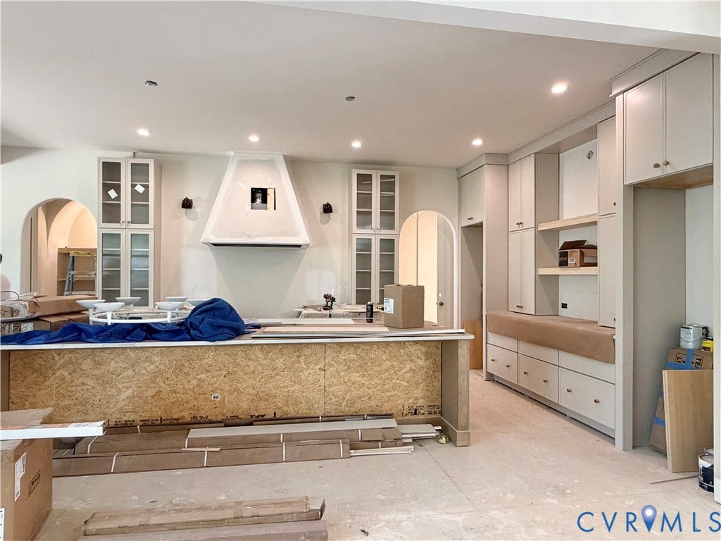 Expansive kitchen featuring custom cabinetry, integrated range hood, recessed lighting, and arched doorways