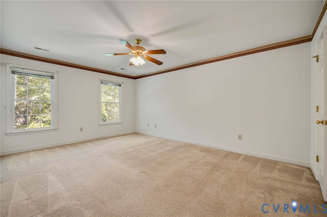 3005 Wiltonshire Drive, Richmond, VA 23233 Spacious room featuring neutral carpeting, two large windows, a ceiling fan with light fixture, decorative crown molding, and a paneled door with brass hardware