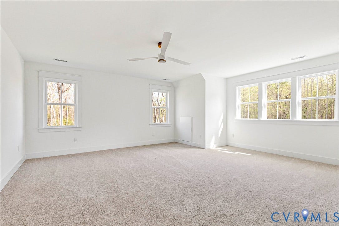 Spacious room featuring light-colored carpeting, white walls, and a modern ceiling fan