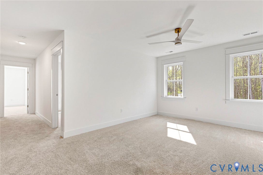 Bright room featuring two windows, light-colored carpeting, a ceiling fan, and white walls