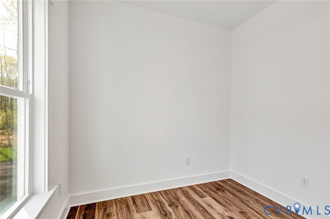 The room features a large window with white trim, white walls, and wood-style flooring