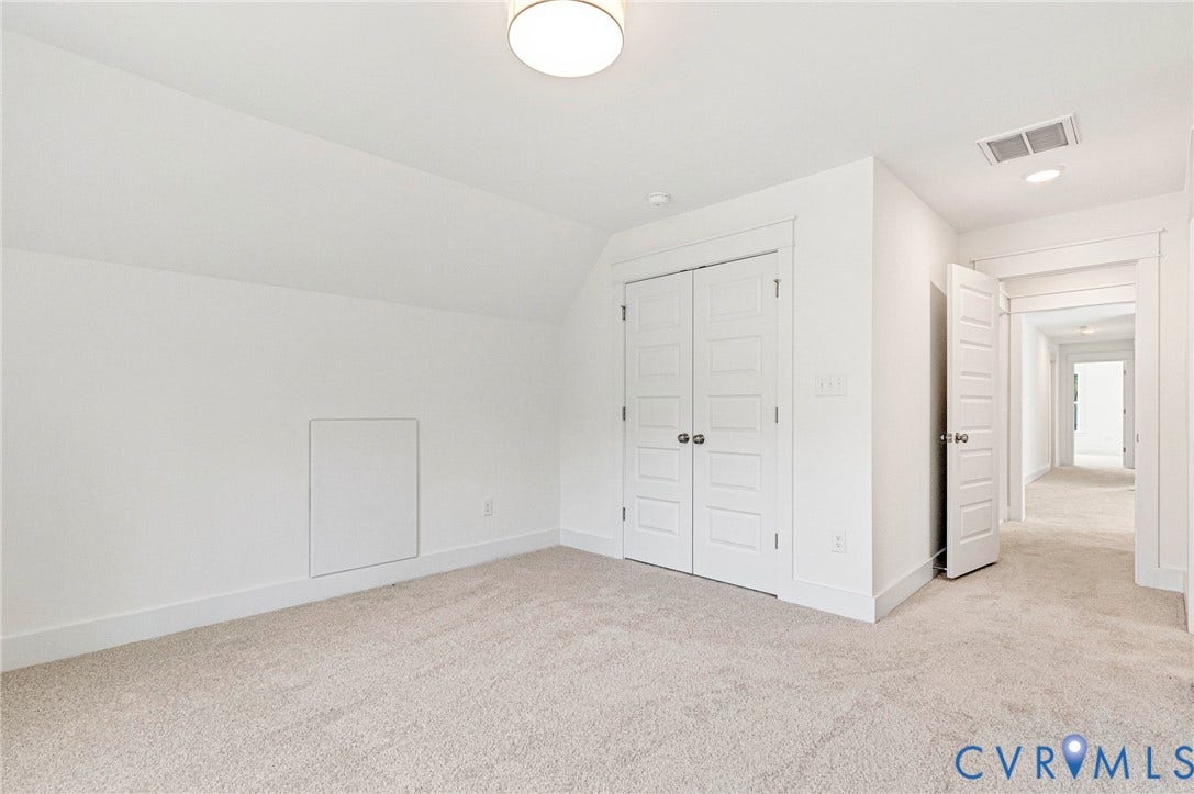 This room features light-colored carpeting, a sloped ceiling, and white walls with white baseboards