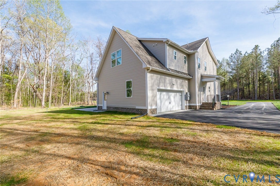 The property features light-colored siding, a multi-car garage, and a long asphalt driveway