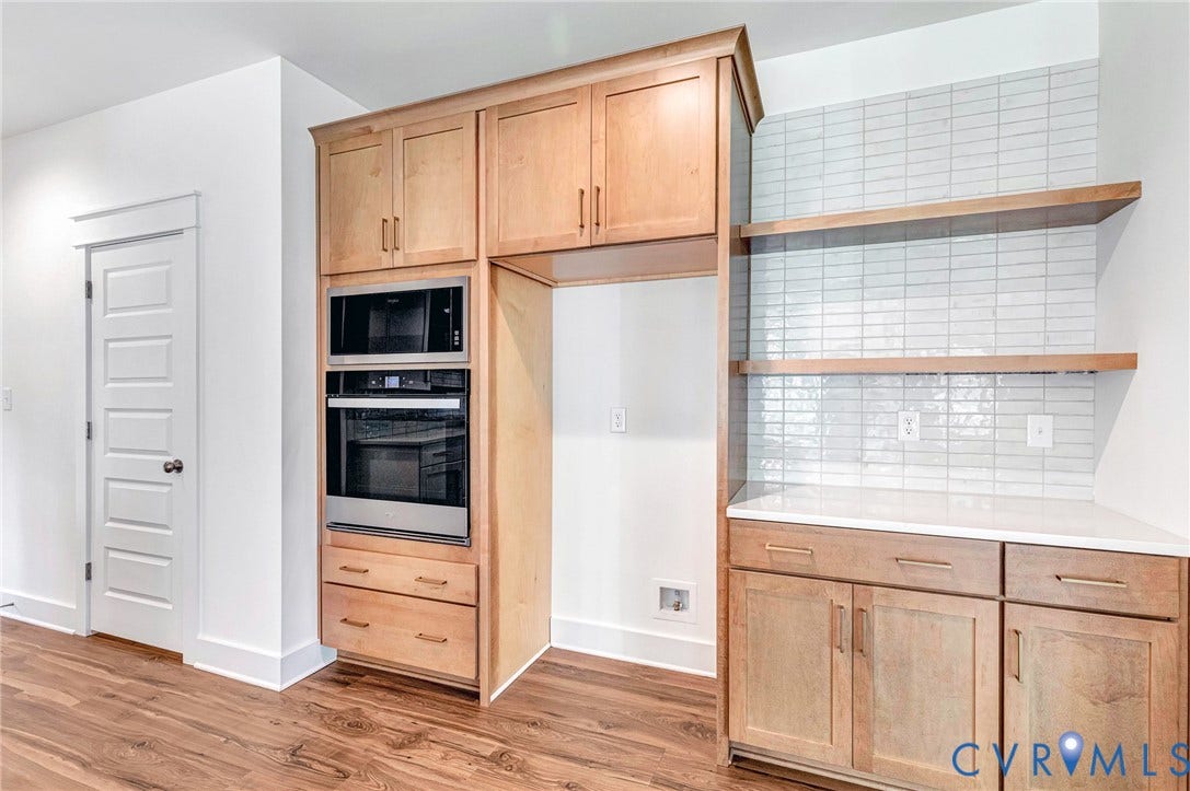 Kitchen area featuring hardwood flooring, light wood cabinetry, stainless steel appliances, and open shelving above a tiled backsplash
