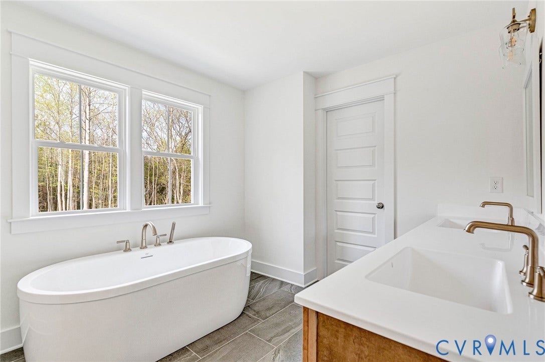 The bathroom features a freestanding soaking tub positioned under two large windows