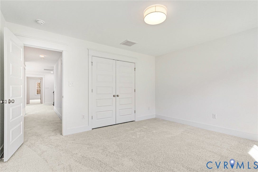 The property features a bright room with light-colored carpeting, a ceiling-mounted light fixture, and white bi-fold closet doors