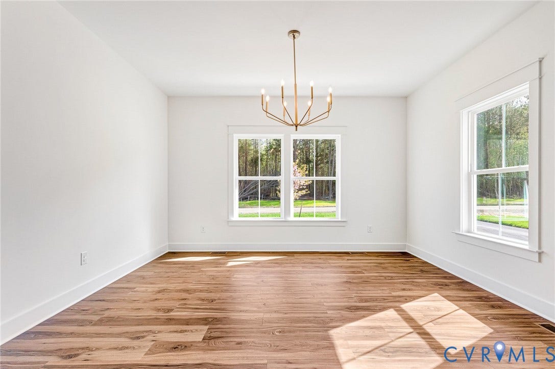 Spacious room featuring light wood flooring, white walls, and large windows providing natural light