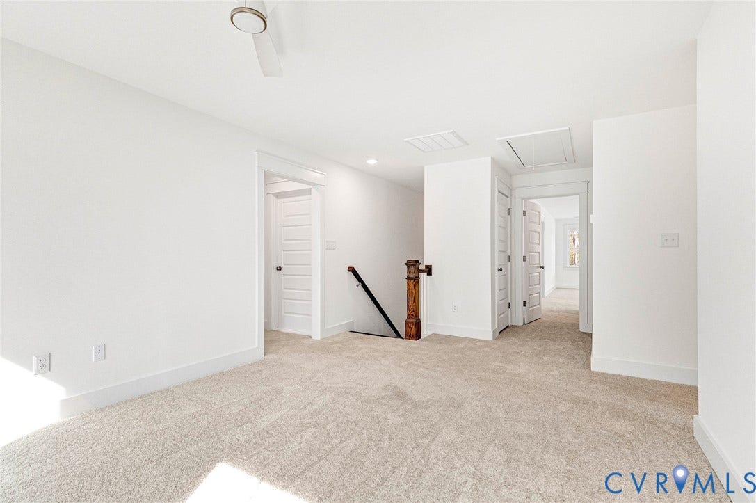 This versatile room features neutral-toned carpeting, white walls, and a ceiling fan