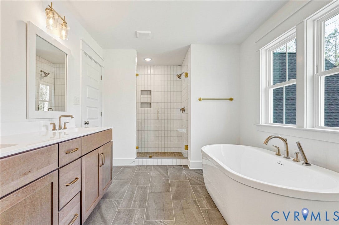 The bathroom features a double vanity with light wood cabinetry, a freestanding bathtub, and a glass-enclosed shower with tiled walls