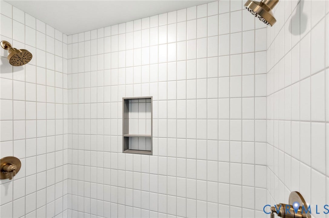 The shower features white subway tile walls, dual bronze showerheads, and a built-in shower niche with shelving