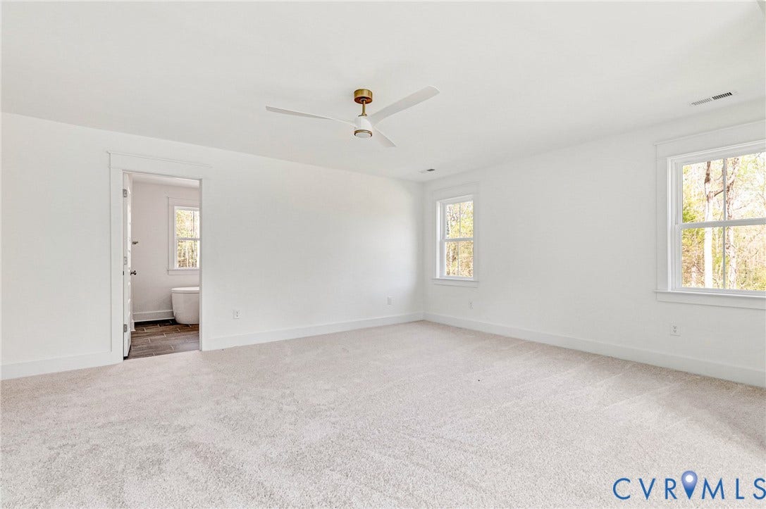Spacious room featuring light-colored carpeting, white walls, and a ceiling fan
