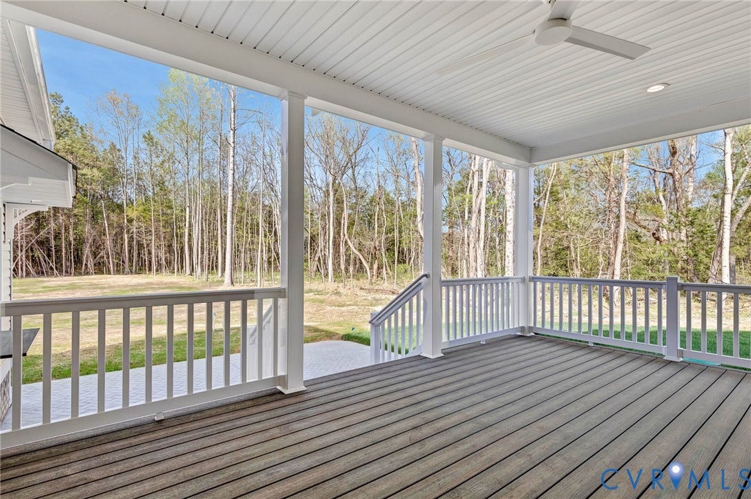 The property features a covered porch with a ceiling fan, offering views of a wooded area and a green lawn