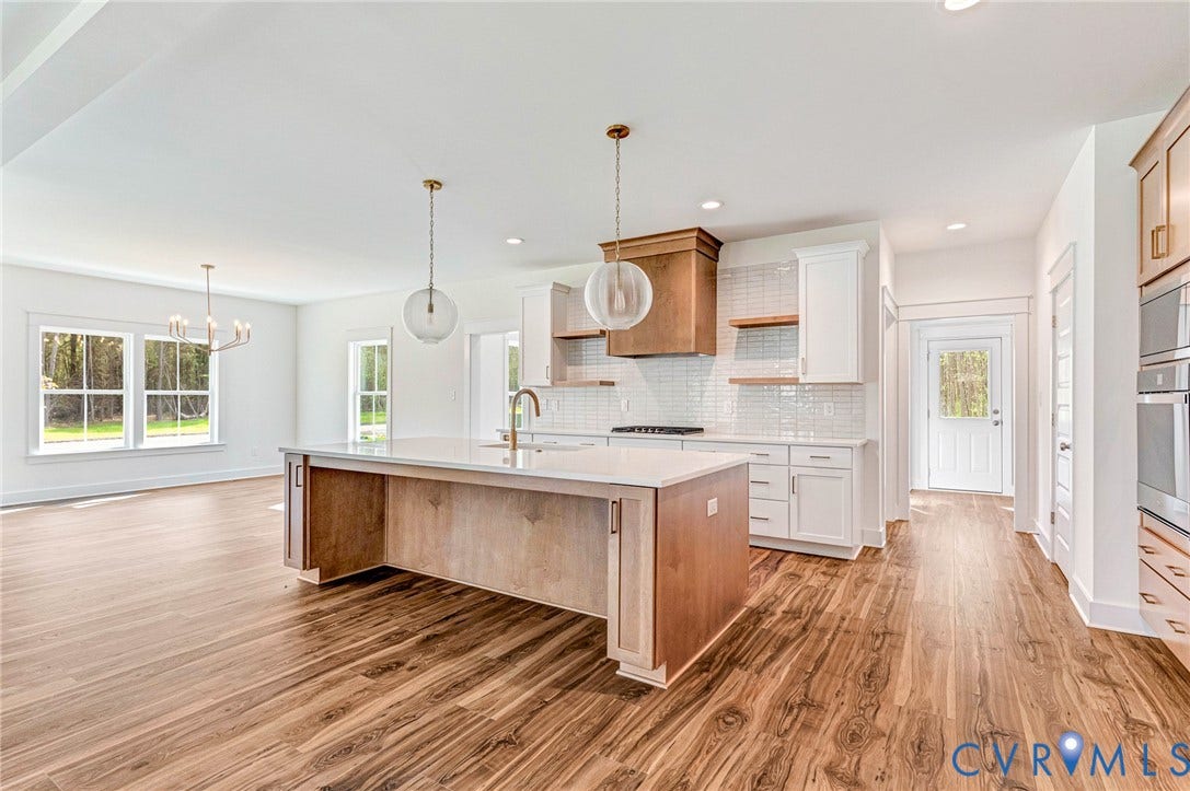 This expansive kitchen and living area features rich wood flooring, a central island with a light-colored countertop, and modern pendant lighting